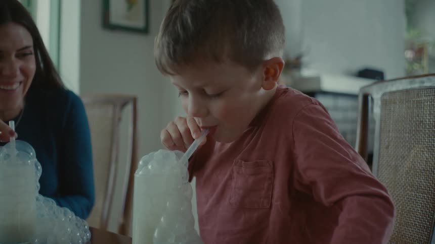 Mother and son having fun making bubbles with glasses of milk