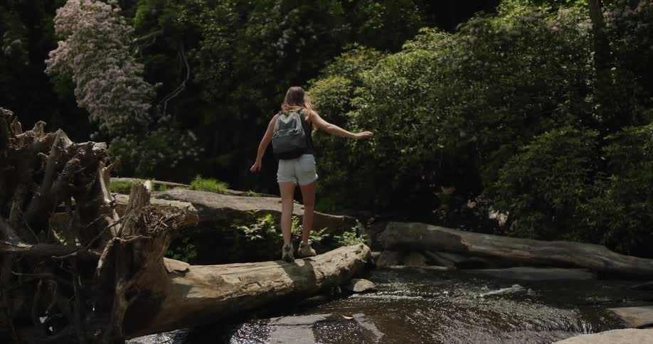 A woman climbs over a log in the stream