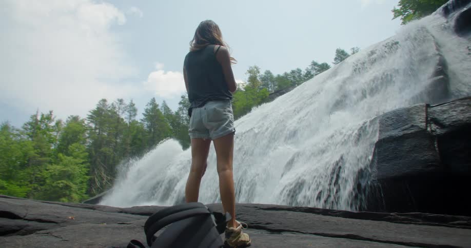 A young woman walks to a waterfall and uses a smart phone to take a picture