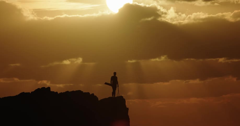 Silhouette of a person on the peak and abyss of a mountain overlooking the sun with the orange sky