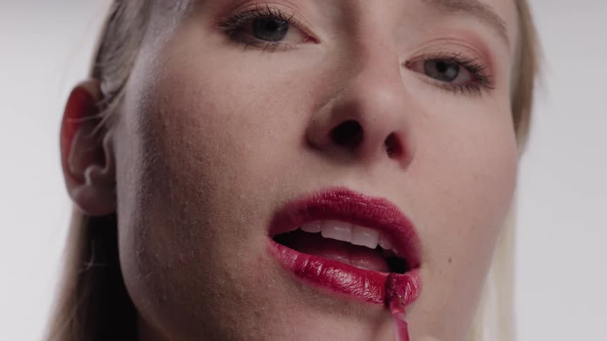 A blonde woman applies lipstick