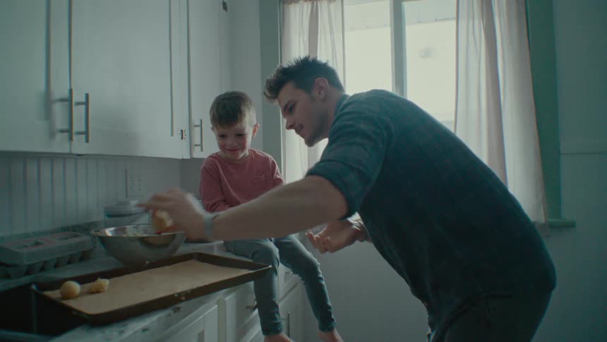 Father rolling cookie dough with his son helping in the kitchen
