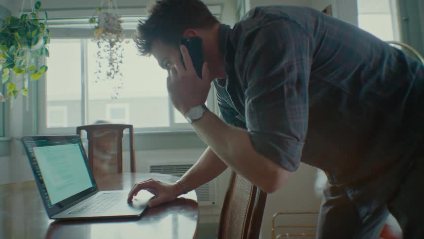 A father works on a laptop and phone while his kids run around playing