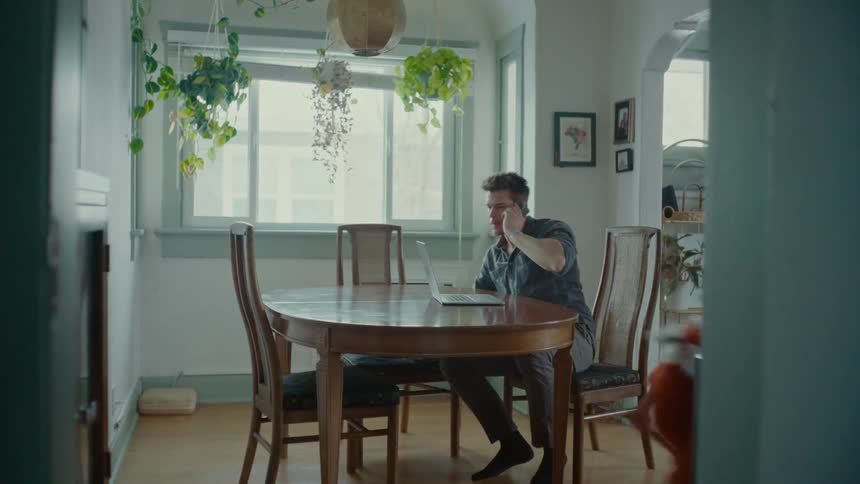 The kids run around a dining room while a man talks on a phone