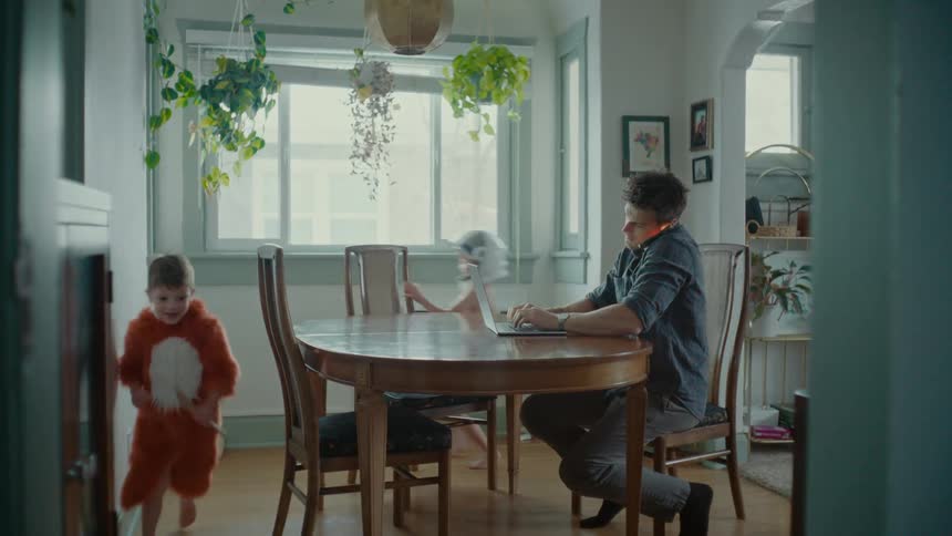 A father sits in the kitchen trying to work with his children playing
