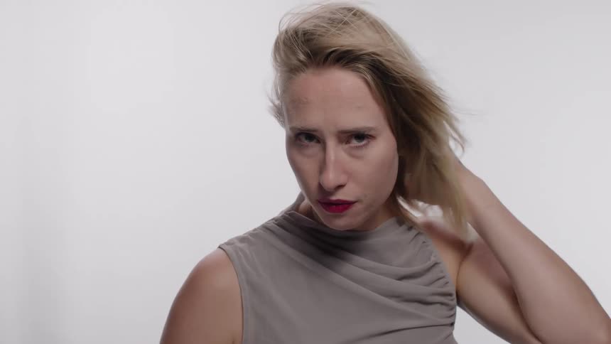 Blonde woman in a studio with a white background posing and adjusting her hair