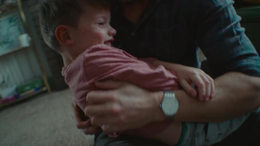 A father playfully tickles his son while in their living room