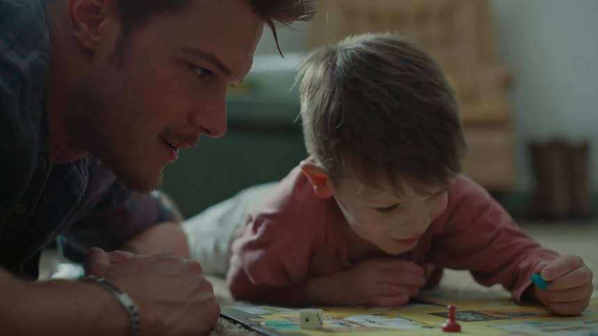 Portrait of the father lying on the carpet with his son while playing a board game