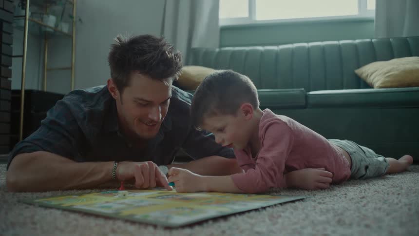 Father lying with his son on the floor rug playing a board game