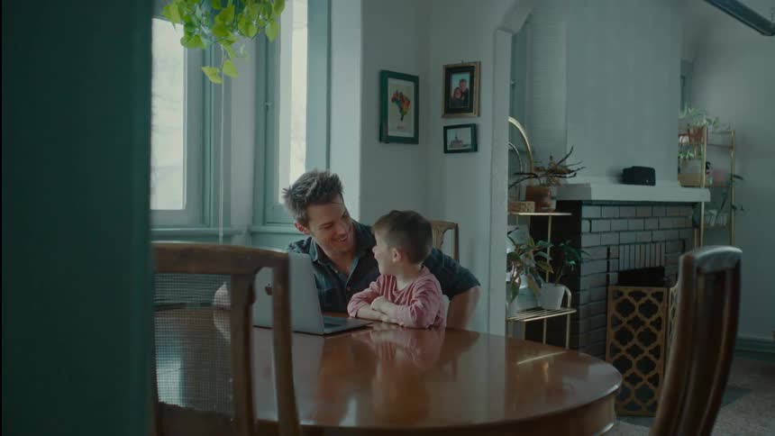 Father sitting with his son at the table both smiling while looking at the laptop