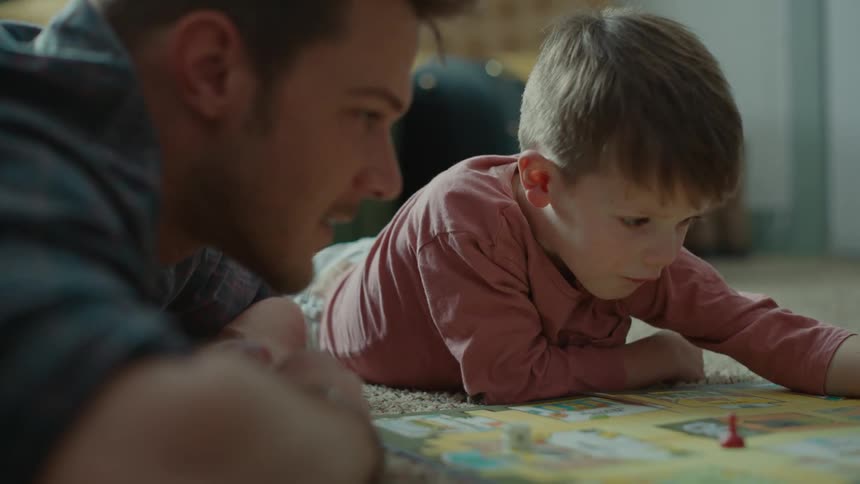 A child and man lie on the floor and play a board game