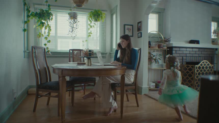 A mom works at a dining room table while her kids run around in circles playing