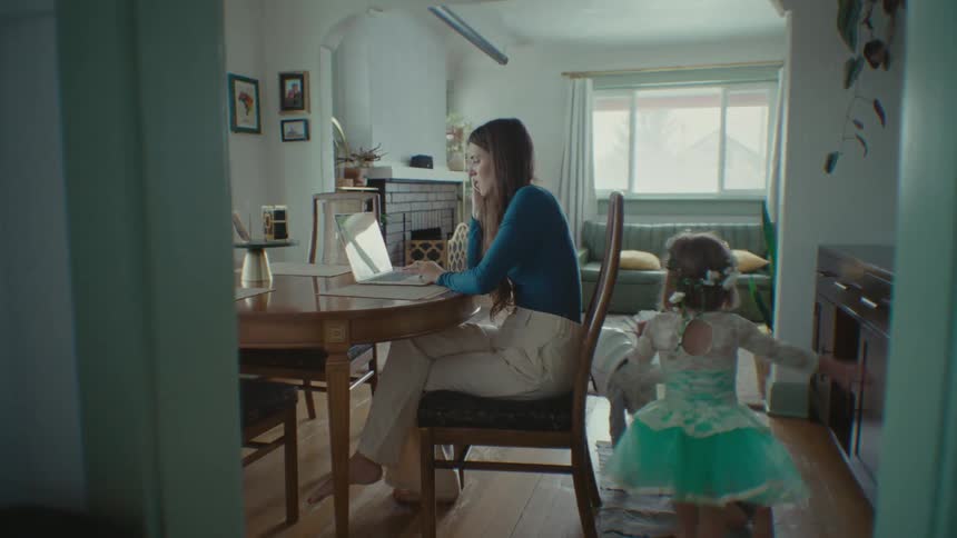 Lady talking on phone while operating a laptop and her children playing around inside the house during the day