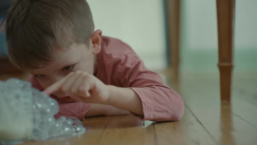 Little boy lying on the floor popping bubbles formed by a glass of milk