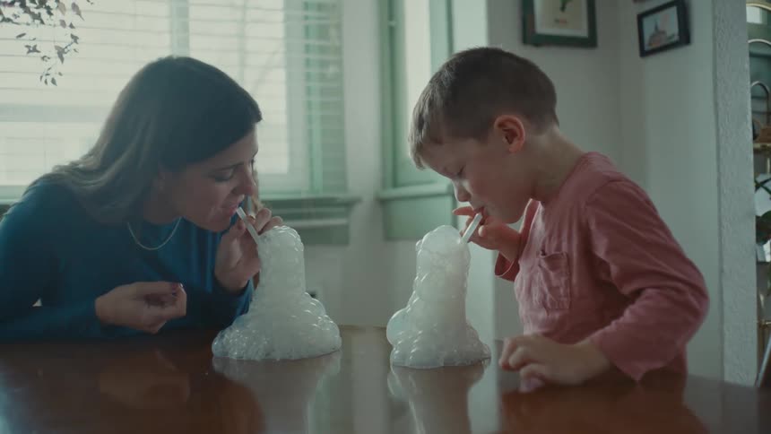 Mother and son playing blowing a straw into a cup that creates foam and bubbles