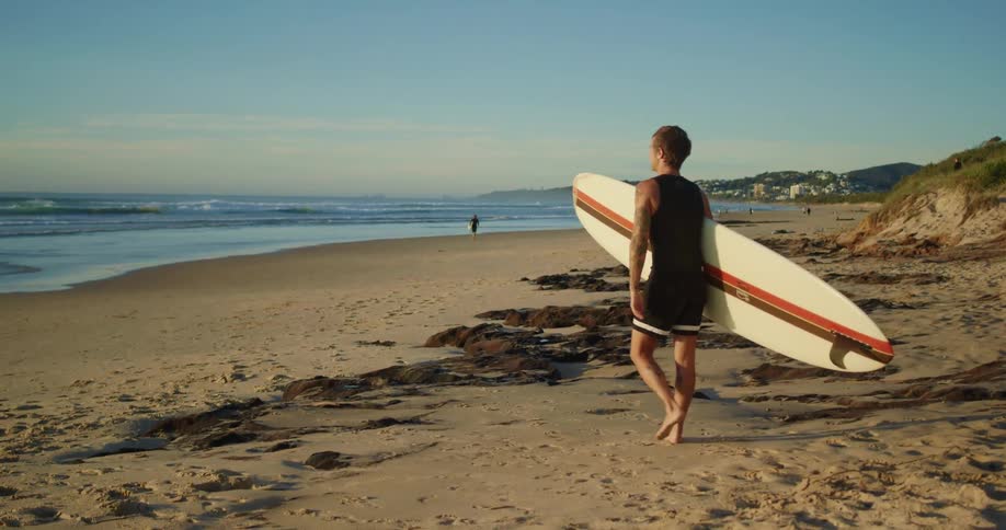 A man carries his surfboard on the beach