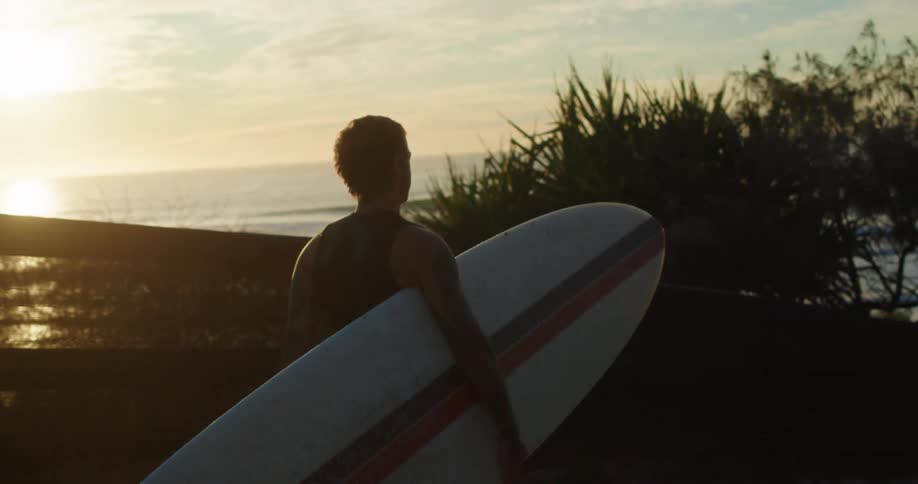 A man with a surfboard walking towards the sea at sunset