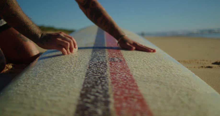 A man rubs a block of wax on a surfboard