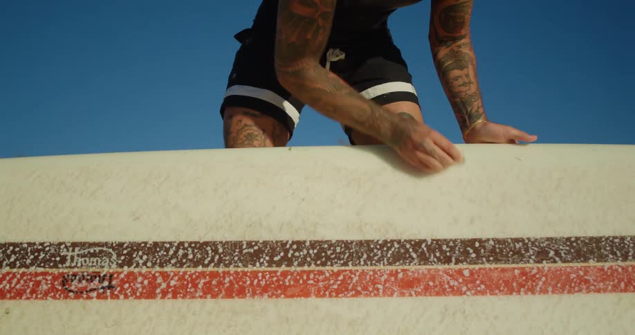 Man waxing his surfboard with paraffin