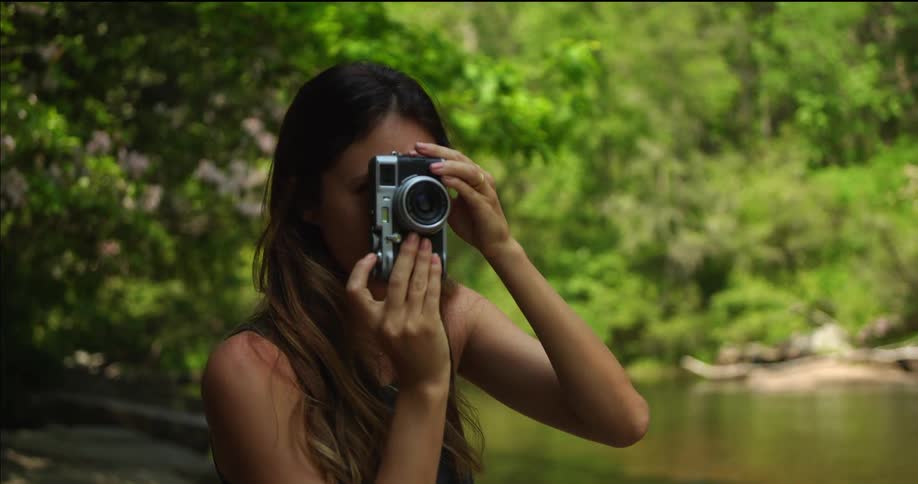 A young woman holds up a camera to her eye to take a photograph while outdoors