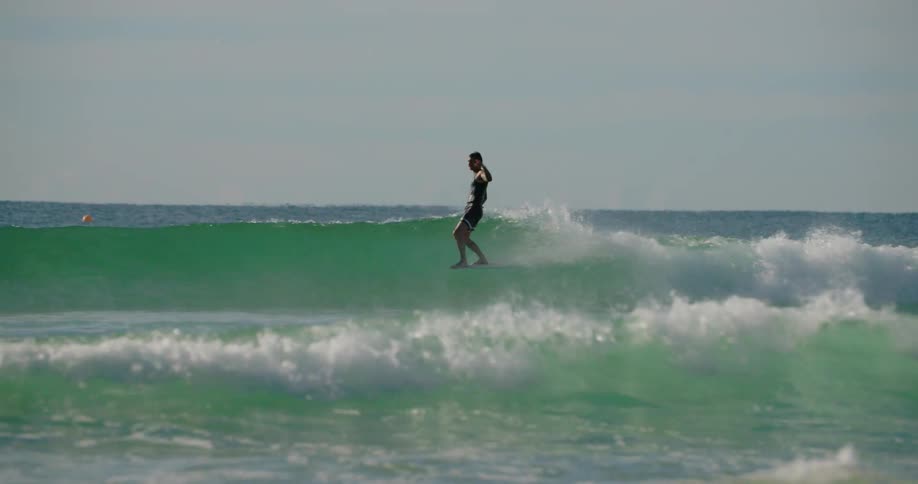 A man surfs an ocean wave and then falls off his surfboard