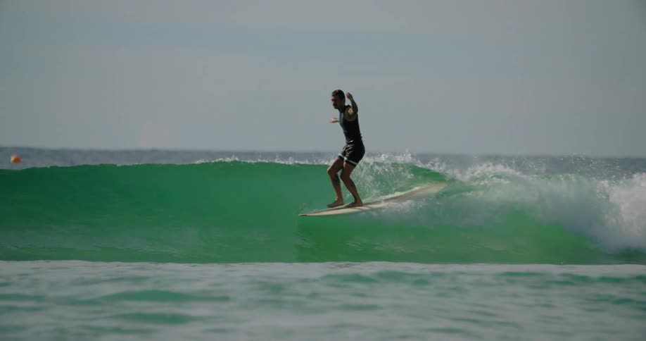 Man riding a small wave with a longboard and falling off