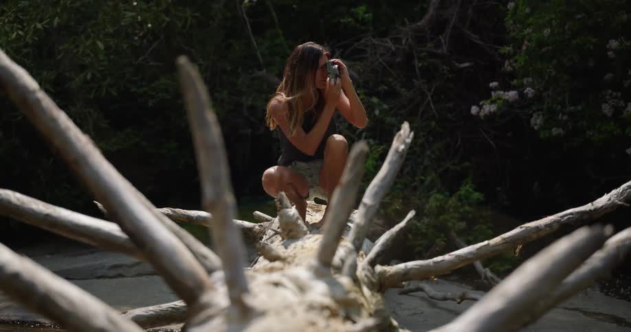 Woman lying on a log near a lake and holding a camera