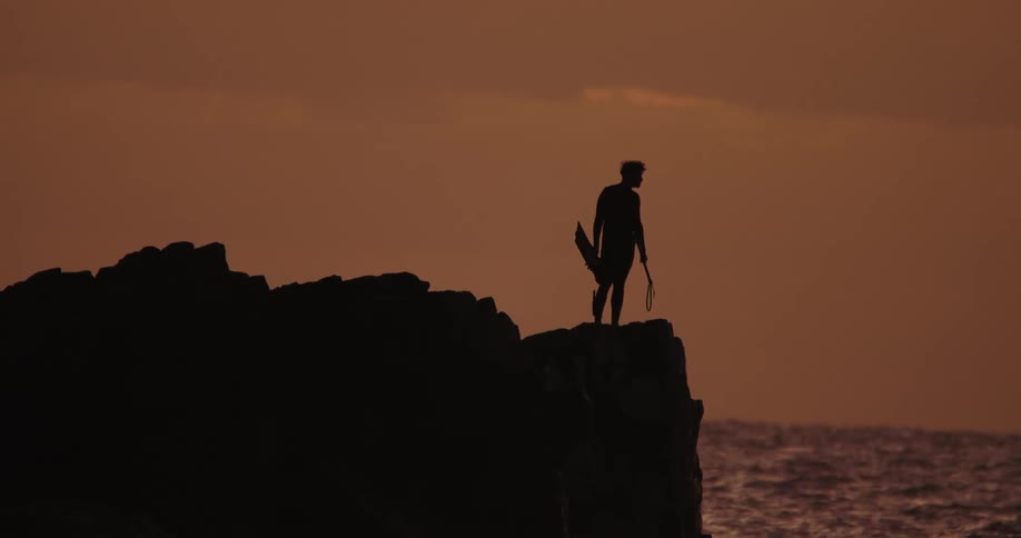 Man on a cliff by the sea with a reddish sky