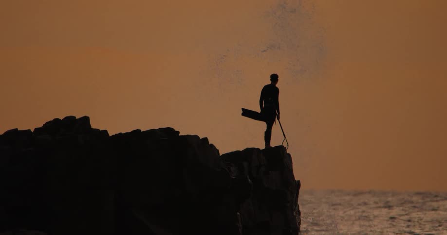 A man is standing by the cliff near the shore
