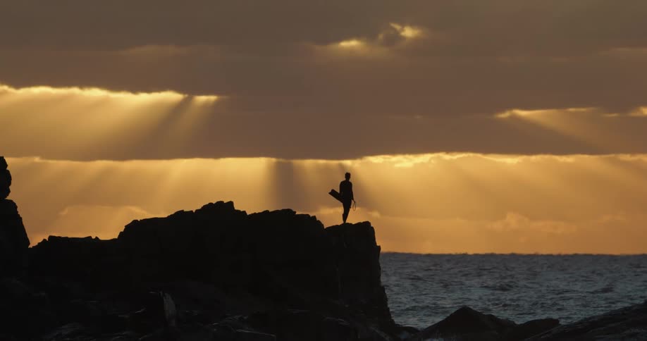 Silhouette of a man on a cliff by the sea on a day with a reddish sky