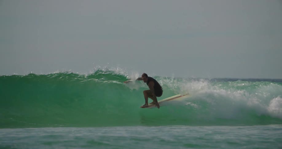Man riding a small wave with a longboard and finishing the ride