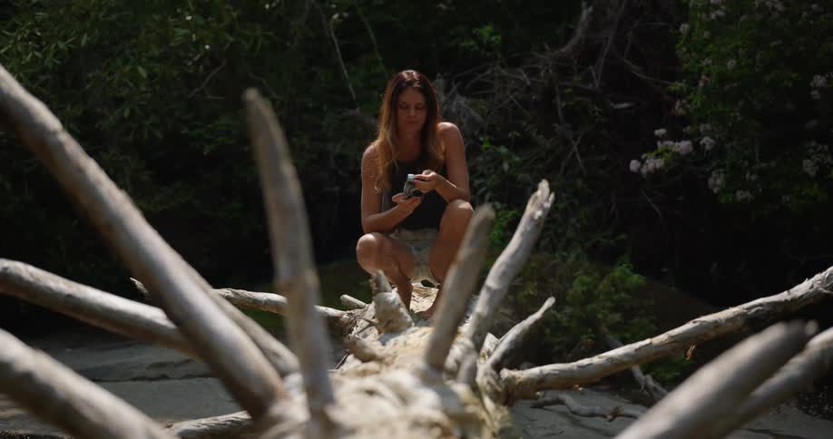 A woman crouches on a fallen tree and takes a photo