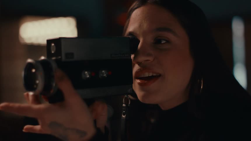 A woman holds a handheld video camera to her eye and makes adjustments to the lens