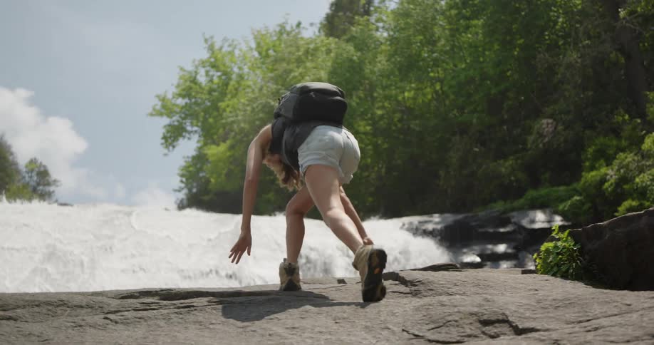 Woman climbing a rock towards a waterfall