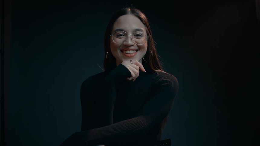 Woman sits in chair smiling against a blue background