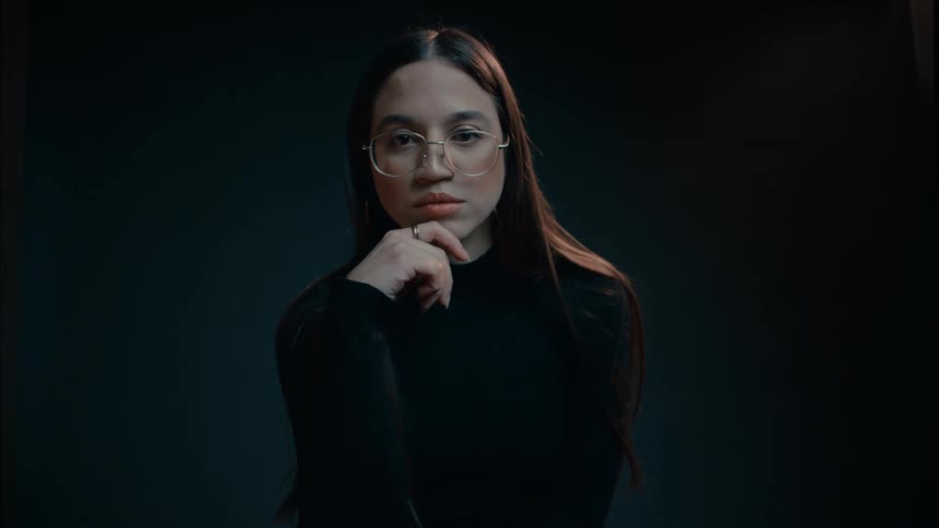 Woman wearing dark clothing crosses her legs and leans on her hand
