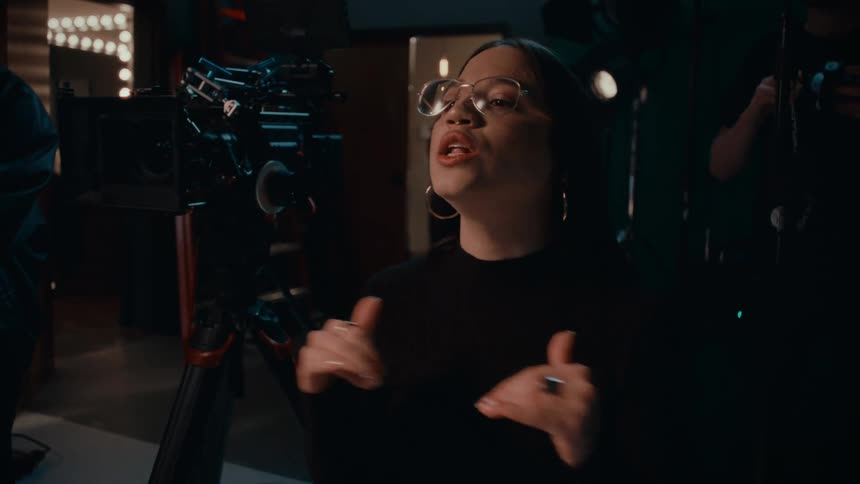 Woman sitting and talking in a studio with low lighting cameras and a crew around her