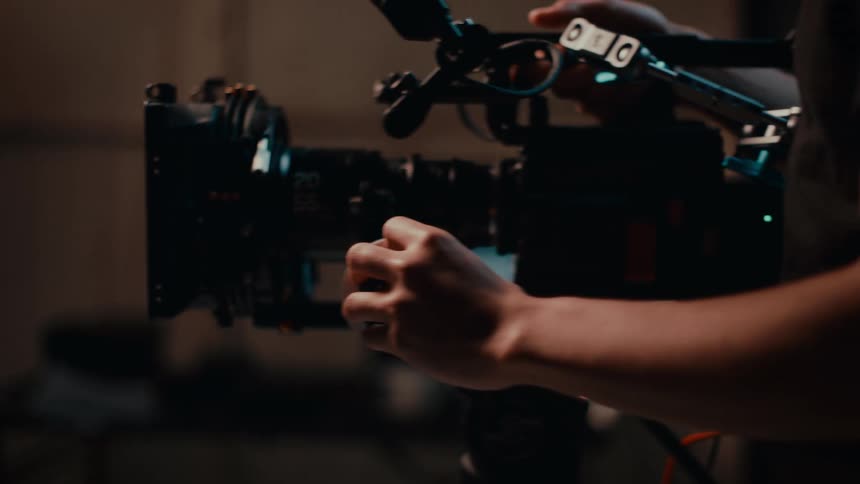 Portrait of a woman talking in a dimly lit room just behind her a camera being adjusted and filming her