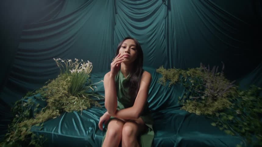 Asian model posing in an armchair in a studio decorated with satin
