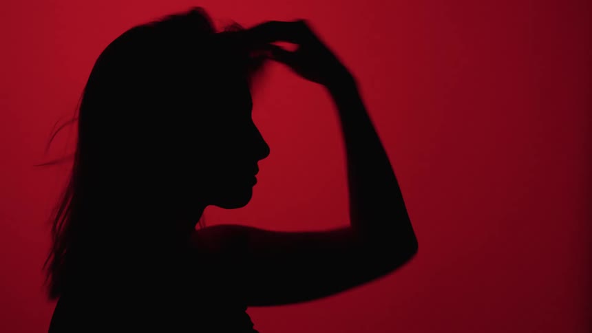 Silhouette of a woman fixing her hair in a studio with a red background