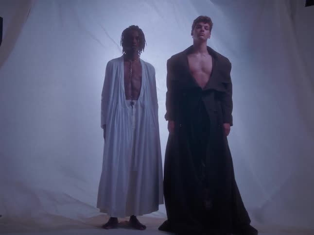 Two male models pose in front of a billowing sheet