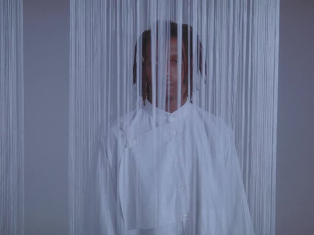Two male models pose in white clothing behind string curtains