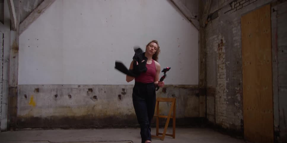 Dancer with curly hair red tank top and black pants picks up smartphone with the tripod