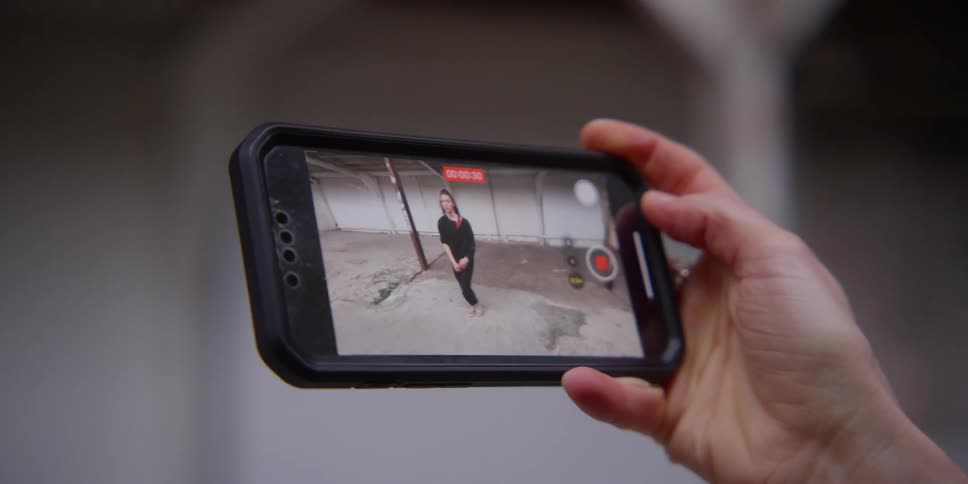 A persons hand holding an iphone and playing a video of a woman dancing