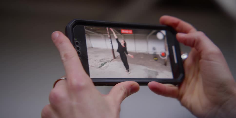 Closeup of a persons hands holding an iphone while a video of a woman dancing is playing