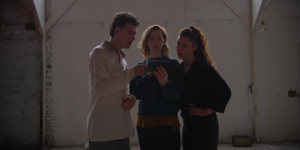 A man and two women look at a smart phone and have a discussion