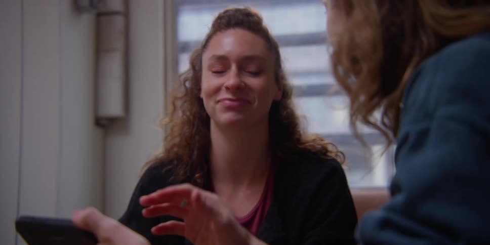 Two women sitting and looking at a smart phone while laughing