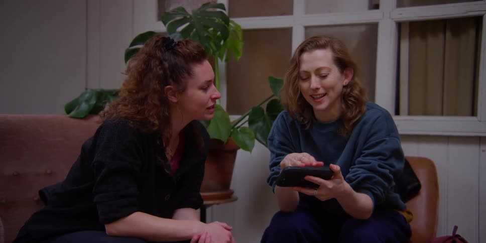 Two women talking while watching videos on their cell phones