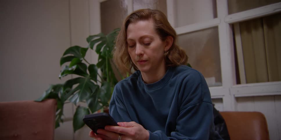 A woman sitting on the couch typing on a cell phone