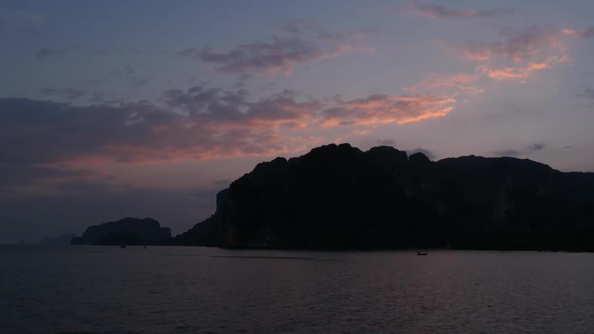 The sun sets behind a large rock and a body of water